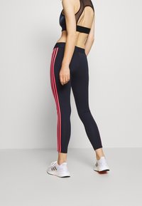 Marina leggings med rosa vertikala ränder, åtsittande design, elastisk midja och kombinerat med vita sportskor. Endast bakvy.