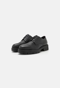 Chaussures en cuir noir avec bout arrondi, design à lacets et semelles épaisses texturées. Style minimaliste avec une finition élégante.