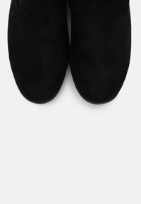 Chaussures en daim noir avec un bout arrondi et des détails cousus, présentant une texture lisse et une semelle plate pour le confort.