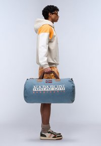 Borsa a tracolla in tessuto azzurro chiaro con manici marroni, che presenta una bandiera norvegese e il logo "NAPAPIJRI geographic" in caratteri arancioni in grassetto.