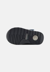 Semelle de chaussure en caoutchouc noir avec une texture striée et un logo circulaire intégré. Présente un motif de grip solide pour une meilleure adhérence.