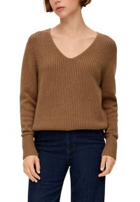 Pull en maille marron texturé avec un col en V et des manches longues, caractérisé par des poignets côtelés et une coupe légèrement ample. Porté avec un jean foncé.
