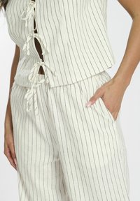 Conjunto ligero de dos piezas en color crema con rayas verticales en azul marino, que presenta lazos en la cintura y el pecho, y bolsillos en los pantalones.