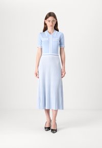 Ljusblå klänning med kort ärm och krage, horisontella ränder på kroppen och en plisserad kjol. Bärs med svarta högklackade skor.