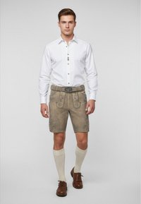 Herroutfit med en vit skjorta med veck, beige lädershorts med blommig brodyr, bruna skor och knähöga strumpor.