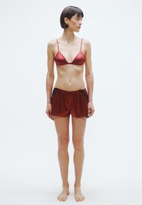 Piros szatén bralette vékony pántokkal, piros rövidnadrággal, fekete csipke díszítéssel. Egyszerű, könnyű kialakítás, testhezálló forma, puha tapintás.