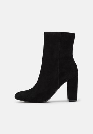 Schwarze Wildleder-Ankle-Boots mit runder Zehenpartie und robustem Blockabsatz. Sie verfügen über eine glatte Textur und ein minimalistisches Design ohne sichtbare Beschläge.