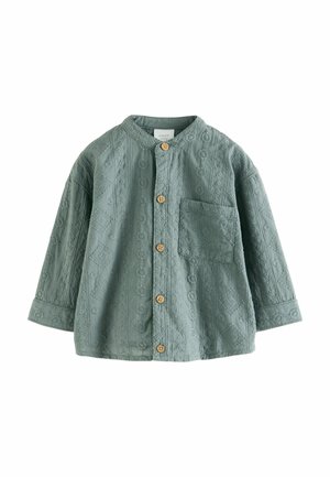 Grünes Shirt mit Struktur, Rundhalsausschnitt, Knopfleiste und einer Brusttasche. Verfügt über komplexe Muster und Holzknöpfe.