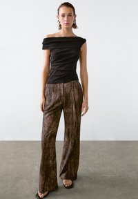 Schwarze schulterfreie Bluse mit tailliertem Design, kombiniert mit braunen, strukturierten, weiten Hosen und schwarzen Sandalen mit metallischen Akzenten.