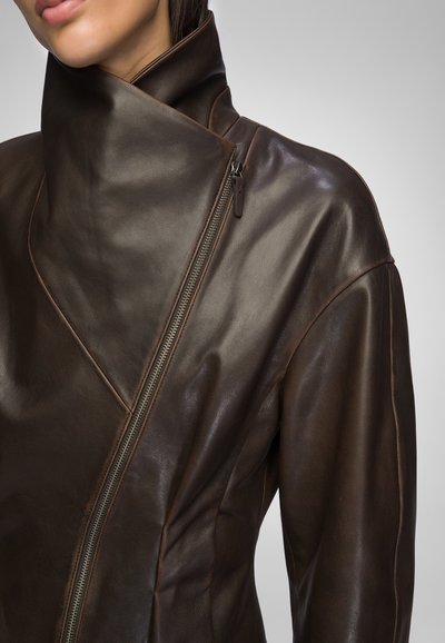 Brown leather jacket with a high collar and diagonal zip closure. Features smooth texture and tailored fit, highlighting craftsmanship.