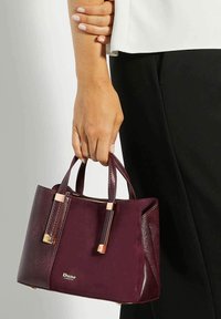 Bordeaux neplederen handtas met twee korte handvatten, gouden hardwareaccenten en een ritsluiting. Textuur body met gladde panelen.