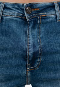 Donkerblauwe denim jeans met contrasterende oranje stiksels en een metalen knoopsluiting bij de tailleband. Heeft een subtiele vervaagde textuur.