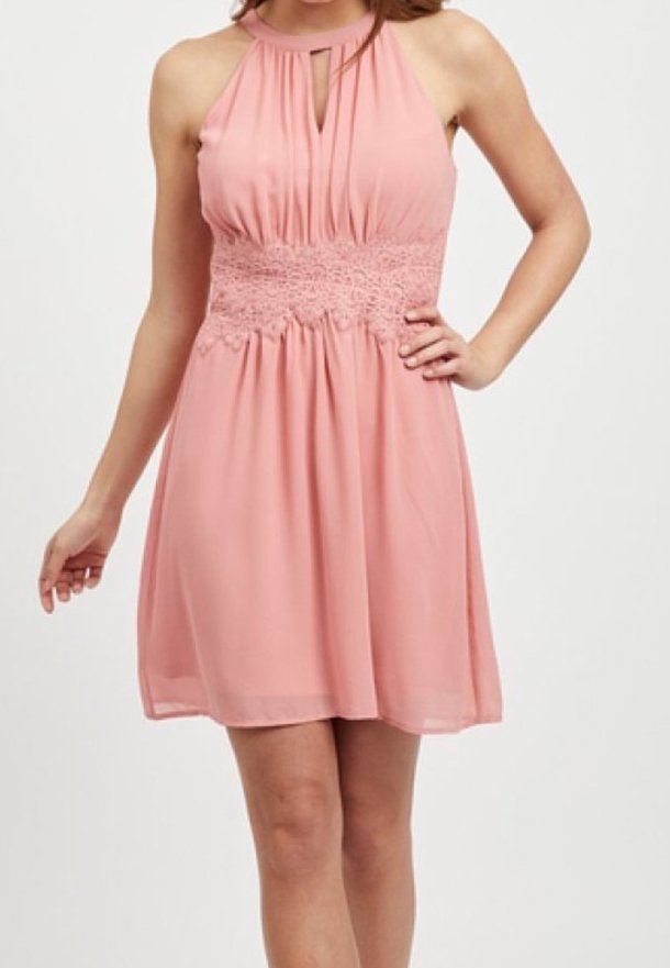 Robe dos nu de couleur rose clair, dotée d'une taille en dentelle texturée et d'un buste plissé. Jupe fluide arrivant au genou en tissu doux et transparent.