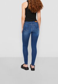 Jeans ajustados en denim azul oscuro, con una cintura de media altura, diseño de cinco bolsillos y una pequeña etiqueta de logo en la parte trasera de la cintura.