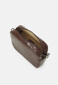 Brązowa skórzana torba o plecionej fakturze, prostokątnym kształcie, podwójnym zamkiem błyskawicznym i gładkim, wyściełanym wnętrzu. Z akcentami w kolorze srebrnym.