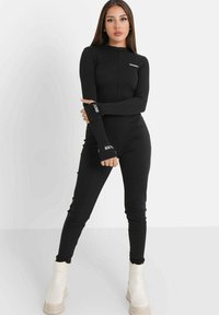 Schwarzer langärmliger Jumpsuit mit Reißverschluss vorne. Verfügt über Textelemente auf den Ärmeln. Glattes, tailliertes Design in einfarbiger Ausführung.