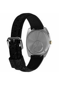 Montre avec un boîtier en acier inoxydable argenté, dos rond, bracelet en cuir noir texturé et boucle en argent. Le dos présente des détails gravés.