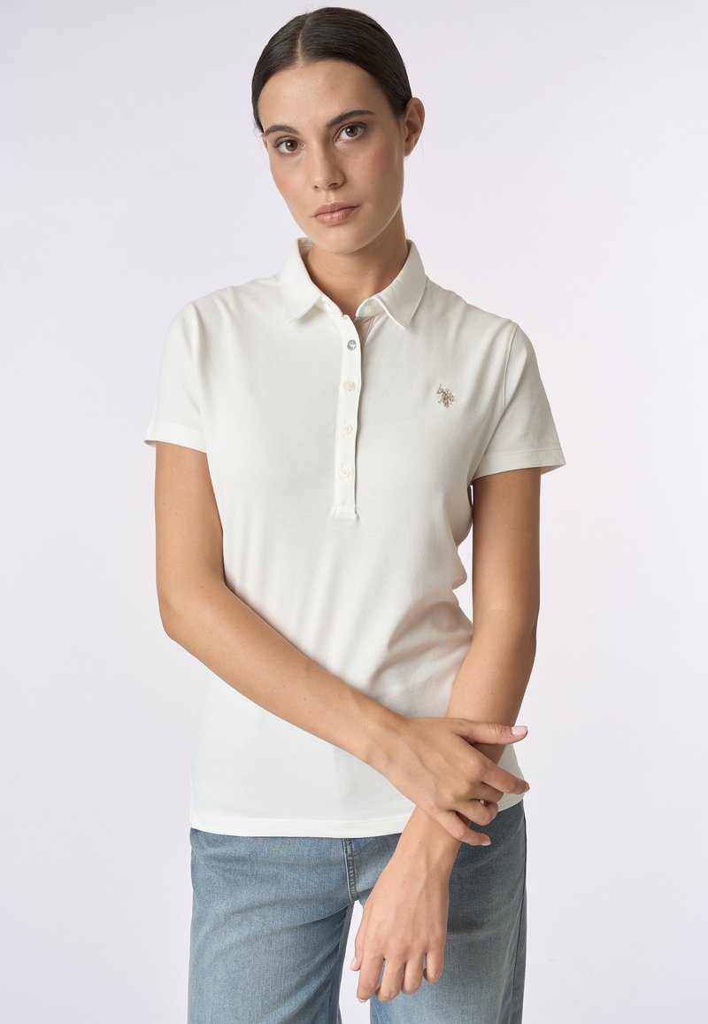 Polo bianco con colletto, maniche corte e patta con tre bottoni. Presenta un piccolo logo ricamato sul petto. Tessuto liscio.