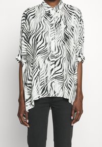 Svart och vit randig knäppblus med krage, lös passform, korta ärmar och asymmetrisk fåll. Slät tygtextur.