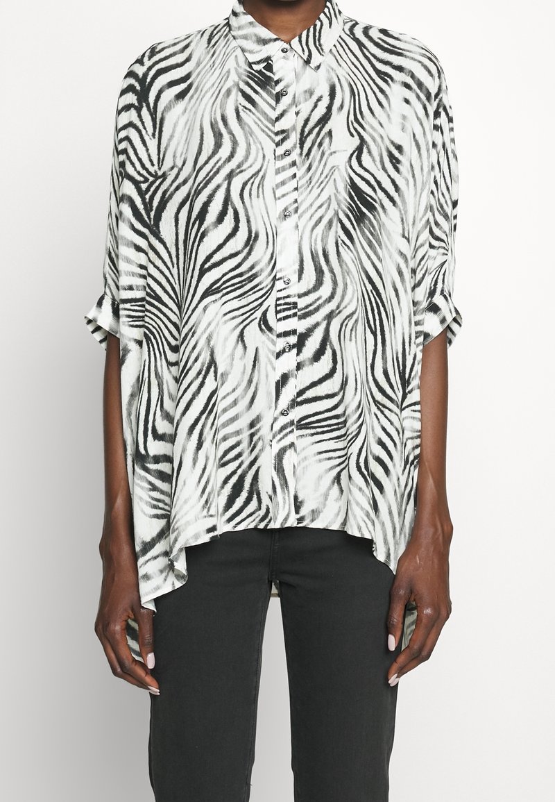 Svart och vit randig knäppblus med krage, lös passform, korta ärmar och asymmetrisk fåll. Slät tygtextur.