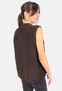 Braun ärmelloses Oberteil aus strukturiertem, flauschigem Material mit abgerundetem Saum und offenen Seiten, getragen über dunklen Jeans.