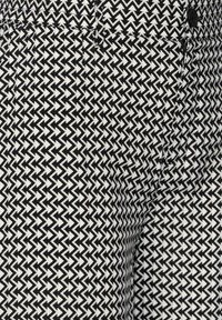 Svart- och vitmönstrad tyg med ett geometriskt zigzag-mönster. Materialet ser slätt ut med synliga sömmar och en svart knappdetalj.