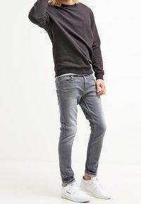Sudadera de cuello redondo gris oscuro, vaqueros ajustados gris claro con textura suave y zapatillas blancas. Conjunto juvenil y casual con acentos mínimos.