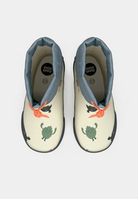 Bottes en crème pour enfants, avec un col rembourré gris, des lacets orange et des imprimés de monstres ludiques verts et noirs sur le dessus, taille 25.