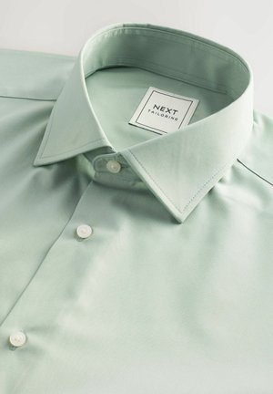 Hellgrünes Hemd mit strukturiertem Kragen, weißen Knöpfen und feiner Textur. Das Etikett trägt die Aufschrift "NEXT TAILORING" in einem quadratischen Design.