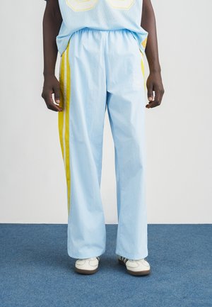 Svetlomodré voľné nohavice s žltými pruhmi na bokoch, elastickým pásom a hladkou textúrou. Kombinované s bielymi teniskami.