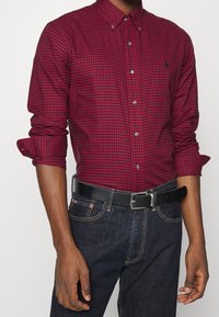 Rood en marineblauwe gingham overhemd met knopen, voorzien van een kraag, lange mouwen en opgerolde manchetten, gecombineerd met donkere denim en een zwarte riem.