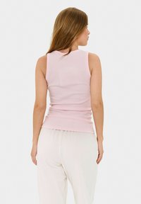 Top senza maniche di un rosa chiaro con un design aderente, texture a coste e orlo dritto, abbinato a pantaloni bianchi larghi.