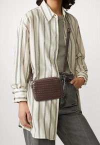 Brązowa pleciona torba na ramię o prostokątnym kształcie, z teksturowanym wzorem, regulowanym paskiem i srebrnymi dodatkami.