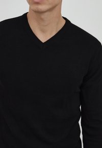 Maglione nero in maglia con design a scollo a V. Presenta un collo a costine e un tessuto testurizzato. Taglio attillato, che mette in risalto il torso.