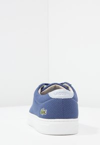 Baskets en toile bleue avec une surface texturée, semelle en caoutchouc blanc et logo crocodile Lacoste sur le côté. Talon renforcé et doublure douce.