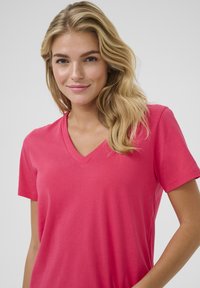 T-shirt rose en V en tissu doux, avec des manches courtes et une coupe décontractée. Design simple sans motifs ni accents visibles.