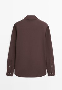 Chemise marron à manches longues avec boutons et col, vue de dos, avec poignets boutonnés sur un fond blanc uni.