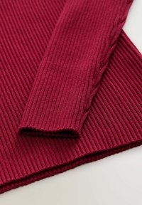 Ribbeliger burgunderfarbener Pullover mit strukturiertem Ärmel und Saum. Verfügt über ein feines Wellenmuster und gestrickte Details entlang der Kanten.