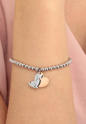 Silver beaded bracelet on wrist with dog and heart-shaped charms, against soft pink fabric background.