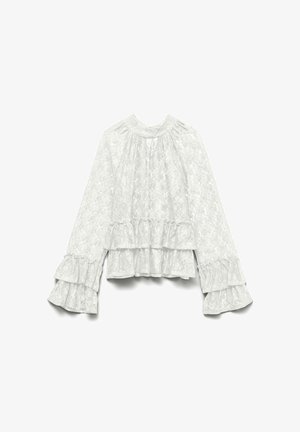 Hvit bluse i blonder med lange, vide ermer og volangkant. Stoffet har et strukturert blomstertrykk med en rynket halslinning.