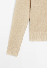 Beige gebreide trui mouw met ribbelmanchetten, zachte textuur en een gelijkmatige steekpatroon. Close-up weergave met focus op de stofdetails en de vorm.