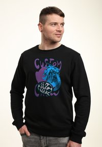 Černá mikina s výraznou grafikou motocyklu a nápisy "CUSTOM" a "BIKE NUT" v fialové a modré barvě. Měkká tkanina a design s kulatým výstřihem.