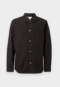 Chemise noire à manches longues boutonnée avec col et poche poitrine comportant un petit logo brodé sur fond blanc.