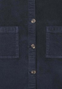 Camisa azul marino con un tejido texturizado, que presenta dos bolsillos en el pecho, cinco botones plateados y el logo de la marca bordado en el bolsillo derecho.