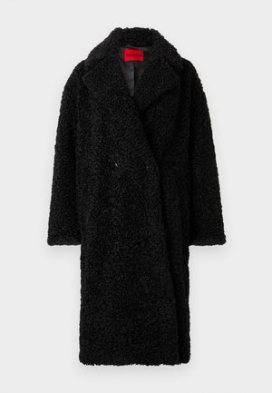 Zwarte lange teddyjas met brede kraag, textuur van krullend stof en een zichtbaar rood "HUGO" label aan de binnenkant van de hals.