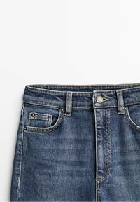 Mörkblå denimjeans med rak passform, fem fickor och detaljer i metall. Ytan är något sliten med en mjuk finish.