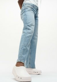 Lichtblauwe denim jeans met een rechte snit en een rafelrand, gecombineerd met witte instappers met ventilatiegaten aan de zijkanten.