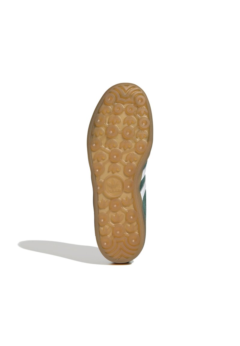 Suola della scarpa in gomma naturale con un motivo testurizzato a pois e rilievi. Parte superiore verde con tre strisce bianche, che enfatizzano il design sportivo.