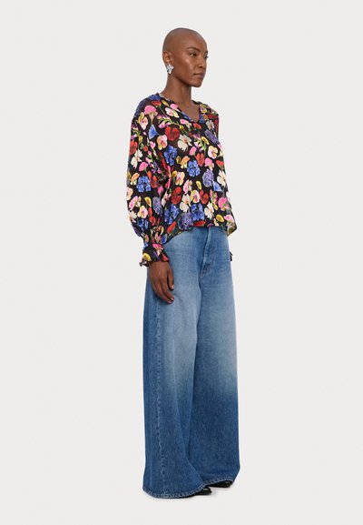 Blusa floreale nera con fiori multicolori, taglio morbido e maniche lunghe; abbinata a jeans in denim a gamba larga di colore azzurro chiaro.