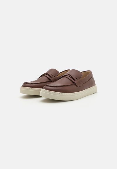 Mocassins en cuir marron avec un design à contours, présentant un détail de couture visible et une semelle en caoutchouc beige clair.